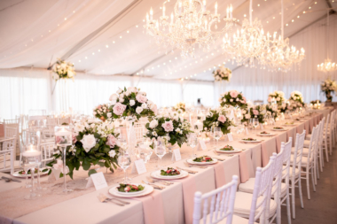 Wedding reception on Sunset Terrace with neutral table linens, greenery and rose arrangements, and crystal chandeliers hung from above