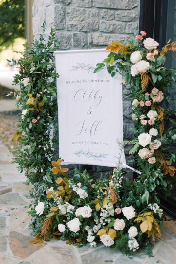 linen hanging welcome sign surrounded by greenery and florals