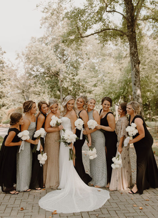 Bride poses with bridesmaids in mansion's cobblestone driveway