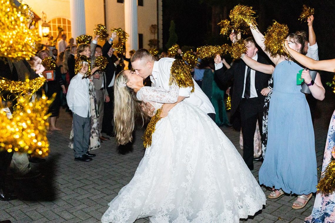 Andrea and Trevor embrace as guests wave gold pom-poms in front of the Estate at Cherokee Dock