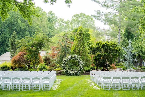 Wedding ceremony setup in Serenity Gardens with white seating and round floral ceremony arch