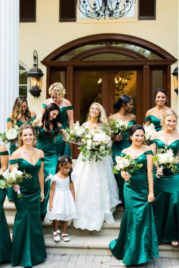 Andrea and her bridesmaid in emerald green dresses pose in front of the Estate at Cherokee Dock