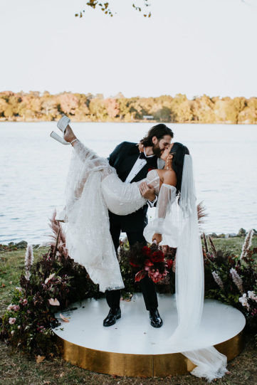 groom holds bride on round platform at the end of the aisle for their lakeside ceremony