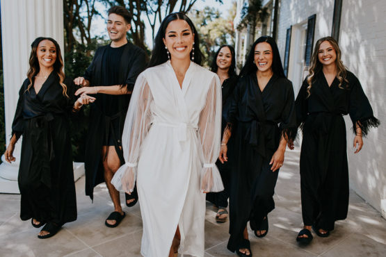 Bride in white bridal getting-ready robe with bridal crew in matching black robes
