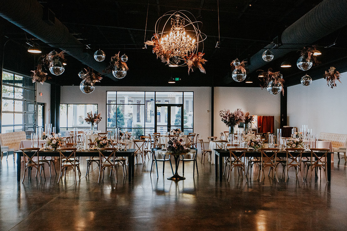 indoor wedding reception with mixed tables and seating with disco balls and boho flower arrangements hanging from the ceiling