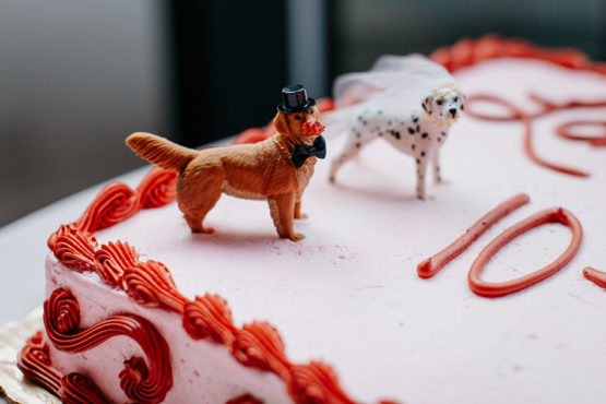 close-up of dog cake toppers on pink sheet cake with red buttercream piping
