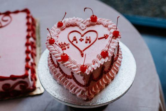 Retro style heart-shaped wedding cake with pink frosting and red piping with maraschino cherries