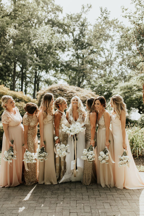 Bride laughs with bridesmaids on cobblestone driveway of mansion