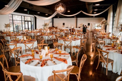 Wedding reception inside Lakeview Event Center with rust goblets and napkins on white linens with wooden crossback chairs