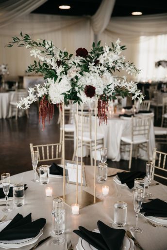 Tall wedding reception centerpiece with bright white blooms and sprigs of greenery on modern gold stand