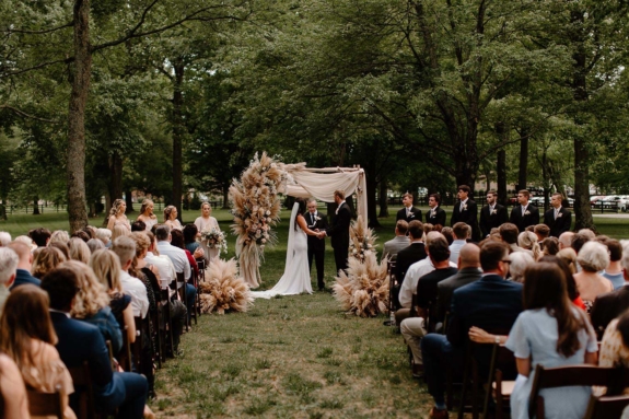 Boho wedding ceremony under the Willow Oak Canopy with large arrangements on drapery-covered ceremony arch