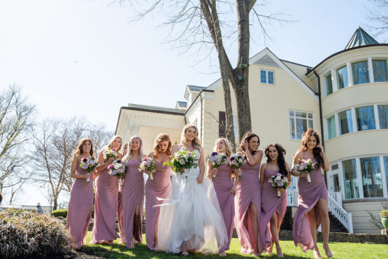 bridal party portrait in front of The Estate at Cherokee Dock Large Wavy Bridal Hairdo with Spring Bouquet and Lace Wedding Dress