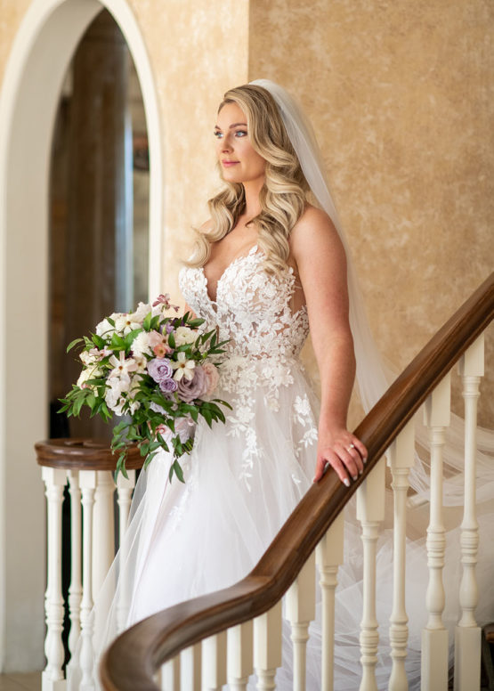 Bridal Portrait on Grand Staircase at The Estate at Cherokee Dock Large Wavy Bridal Hairdo with Spring Bouquet and Lace Wedding Dress