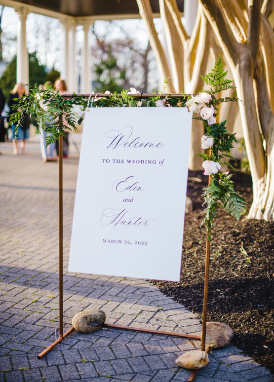 Black and White Signage in Copper Metal Frame with Purple Rose Floral Arrangements and Greenery