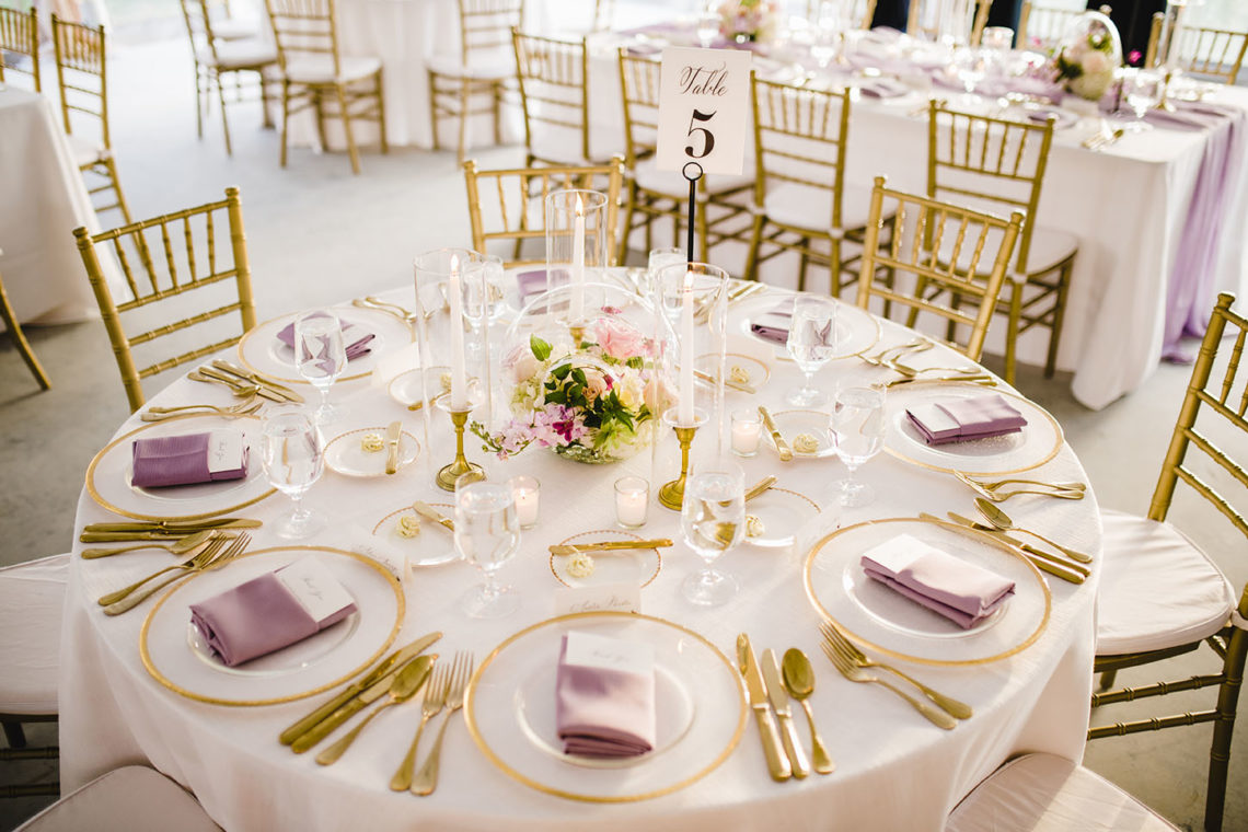 Bright and Airy Wedding Tablescape with Neutral White Linens Purple Napkins Gold Details, and Bright Colorful Spring Floral Centerpieces