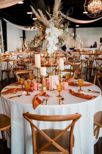 Wedding reception table with tall boho centerpiece arrangement and warm rust-toned decor