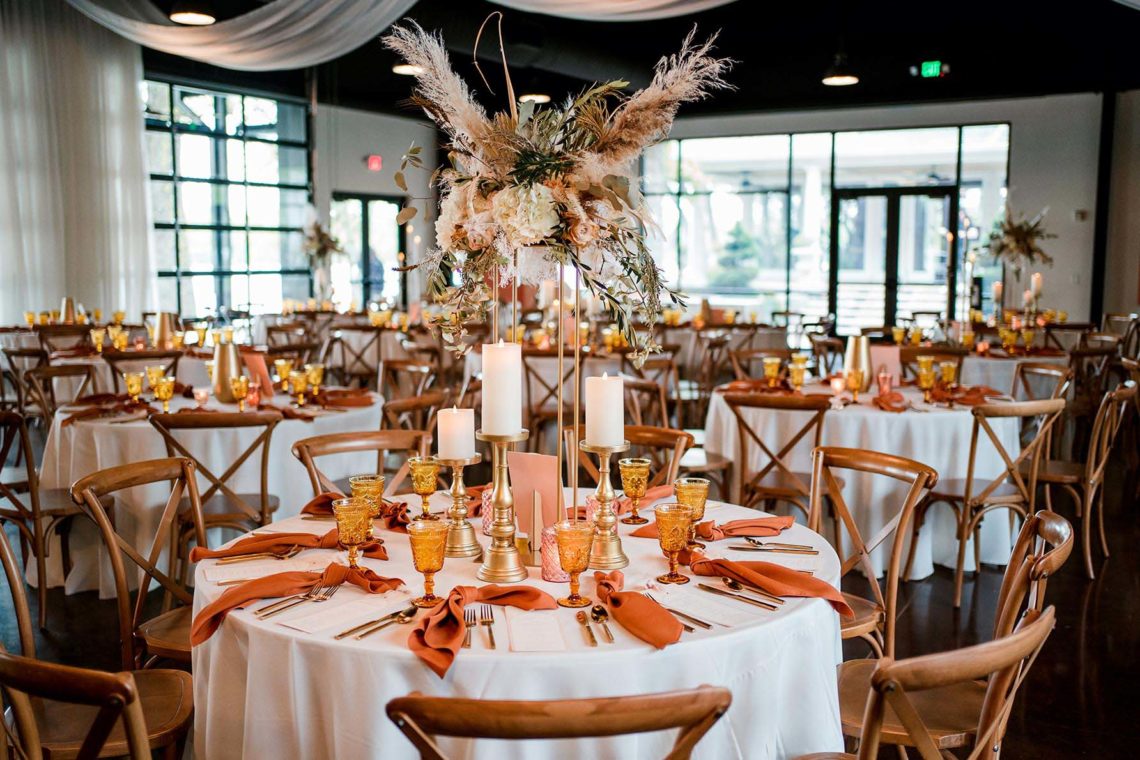 Wedding reception table with warm rust-colored decor and tall wild boho centerpiece