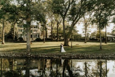 Bride and Groom Standing on Lakeside Lawn of luxury wedding venue with a view, pool, and accommodations