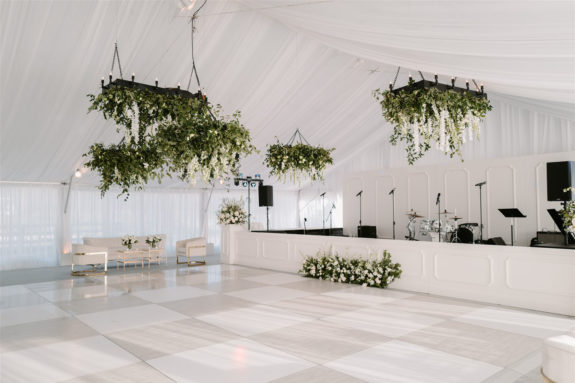 sunset terrace set with white draping a dance floor and custom stage along with hanging greenery installations and white lounge furniture set ups