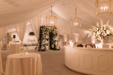 sunset terrace set with white draping a dance floor and custom stage along with hanging greenery installations and white lounge furniture set ups and a circle bar set in the middle