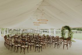 Ceremony setup on Sunset Terrace with brown crossback chairs and round greenery ceremony arch
