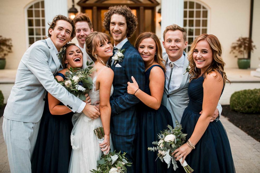 Bride and groom pose with groomsmen and bridesmaids in front of mansion