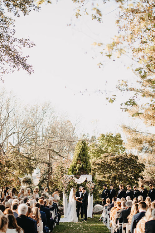 Romantic wedding ceremony in Serenity Gardens with white drapery ceremony arch