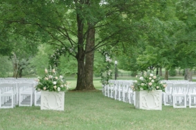Wedding ceremony setup with white chairs, large floral arrangements, and simple arch under Willow Oak Canopy