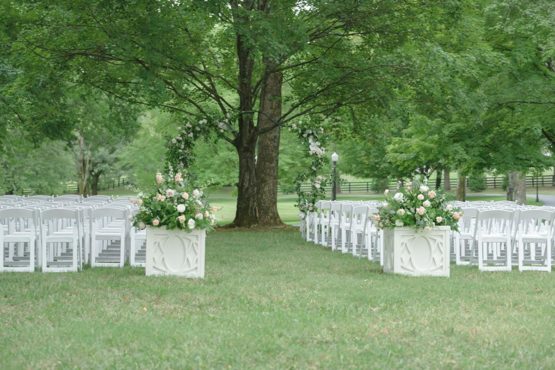 Ceremony set up in the willow oak canopy with white chairs and a greenery arch