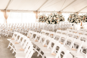 Wedding ceremony setup with white chairs and large white arrangements on tall acrylic stands