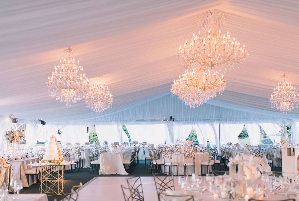 Wedding reception in Sunset Terrace with white drapery covering the ceiling, large crystal chandeliers and tables dress with white linens and white flowers