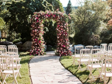 Ceremony arch covered in greenery and pink flowers in Serenity Gardens