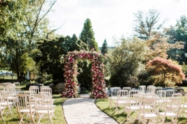 Ceremony setup with floral arch and white chairs in Serenity Gardens