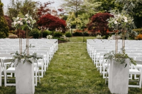 Tall flower arrangements with greenery in white marble planters at top of wedding ceremony aisle