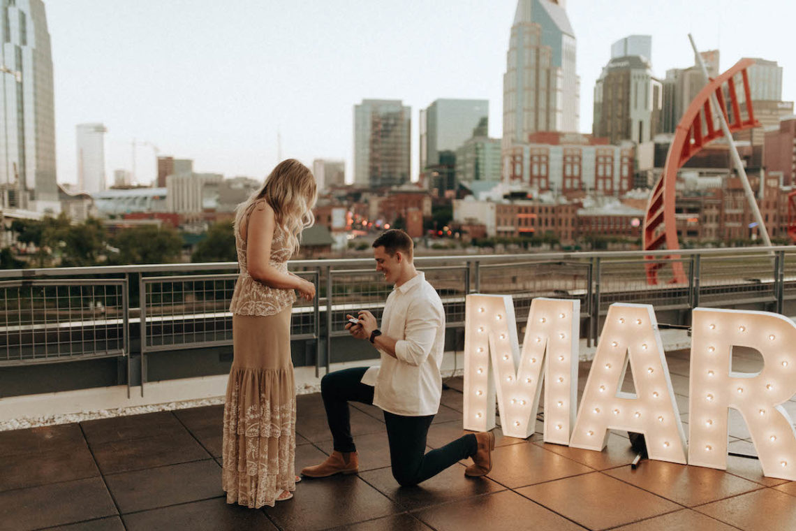 Man proposing to woman on riverfront patio of The Bridge Building in downtown Nashville